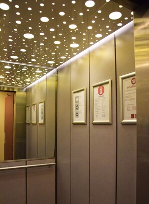 An elevator interior with metallic walls, ceiling lights, and informational signs. - City Apartments Antwerp (Antwerp)