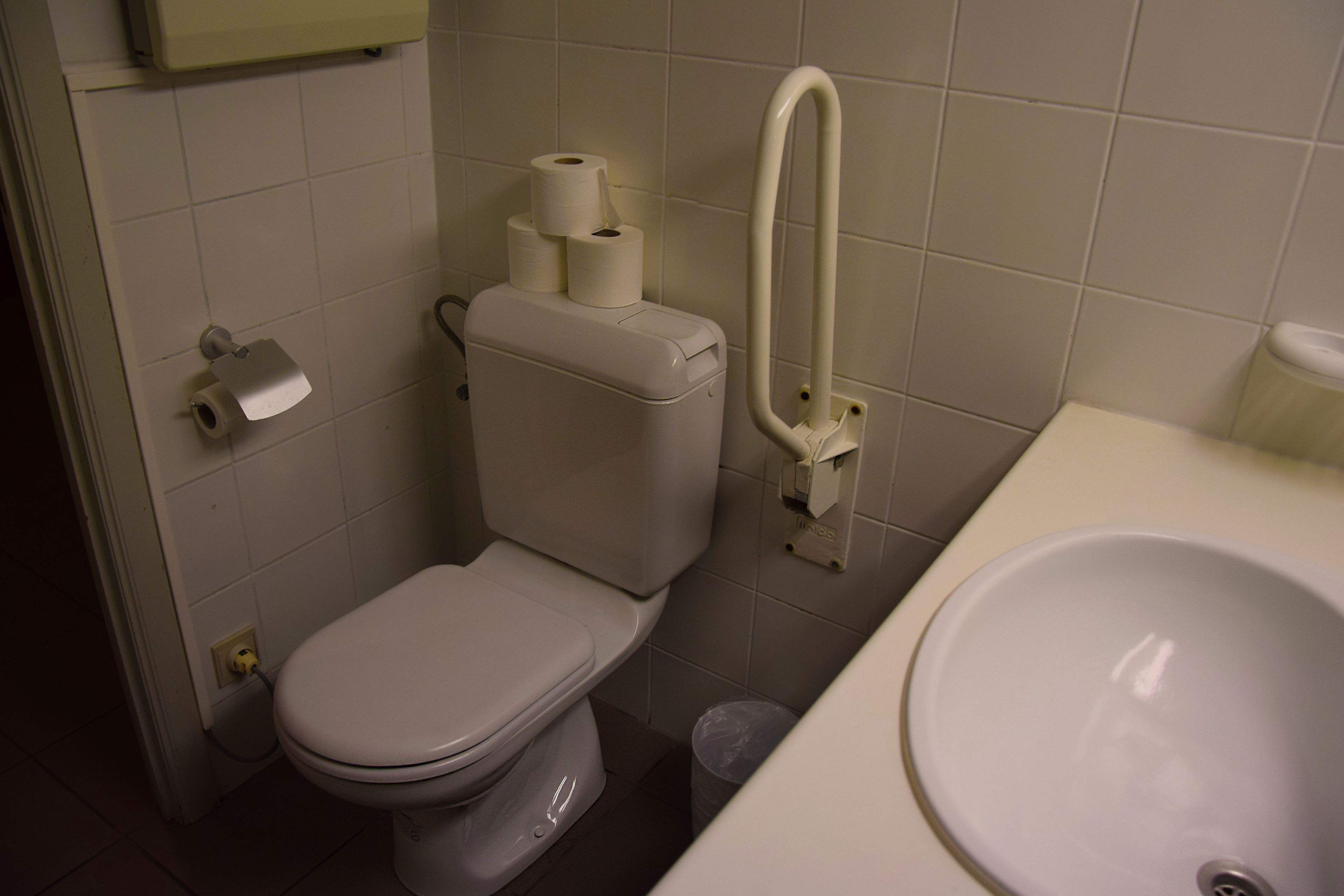 A bathroom with a toilet, a sink, and a trash bin.