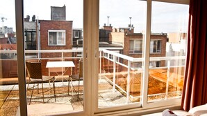 A balcony with a table and chairs, a bed with a rolled towel, and a view of the cityscape. - City Apartments Antwerp (Antwerp)
