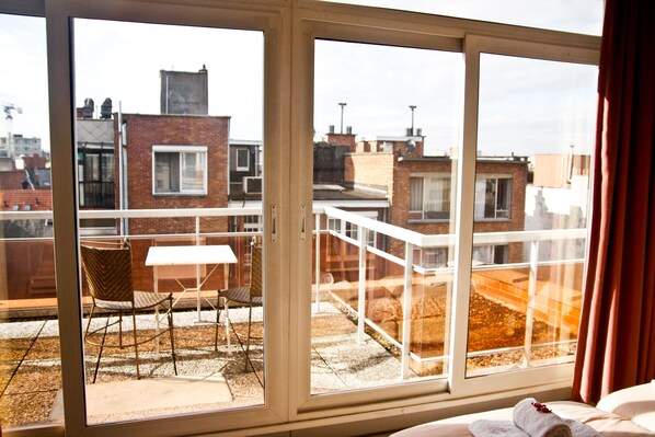 A balcony with a table and chairs, a bed with a rolled towel, and a view of the cityscape. - City Apartments Antwerp (Antwerp)