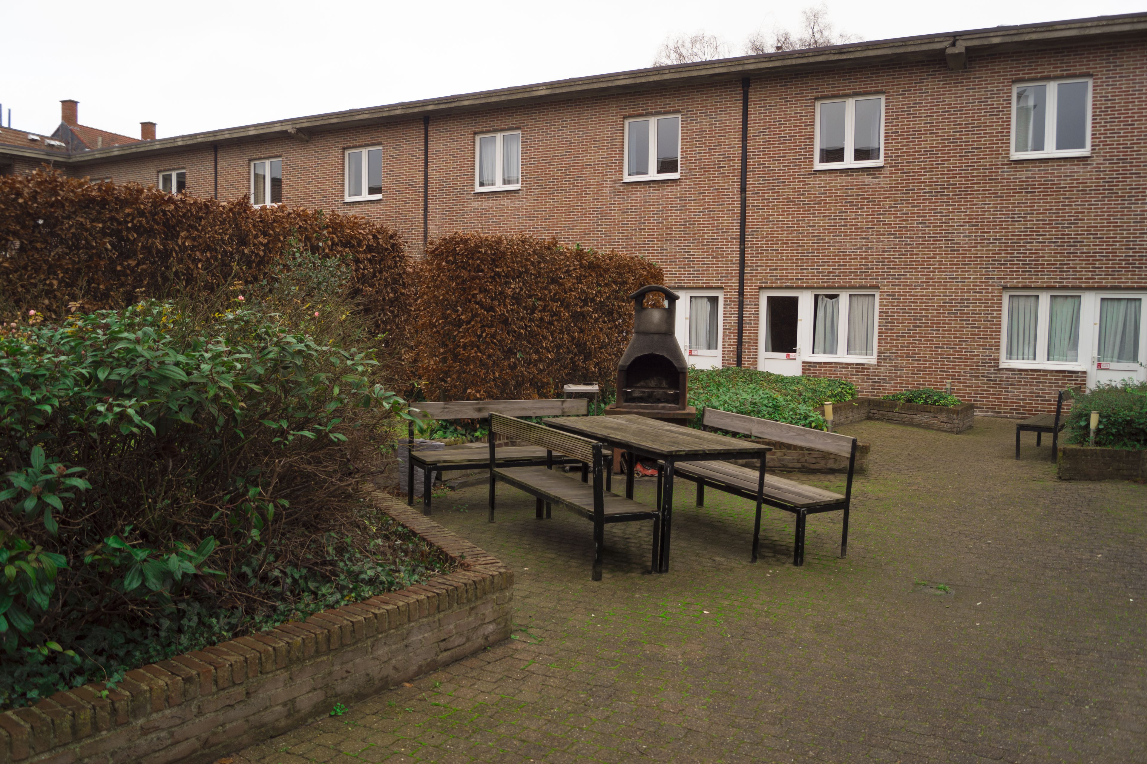 Un cortile con un edificio in mattoni, posti a sedere all'aperto e un'area barbecue.