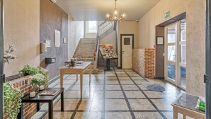 A spacious hallway with a staircase, a display table with postcards, and a chandelier. - Budget Flats Leuven (Leuven)