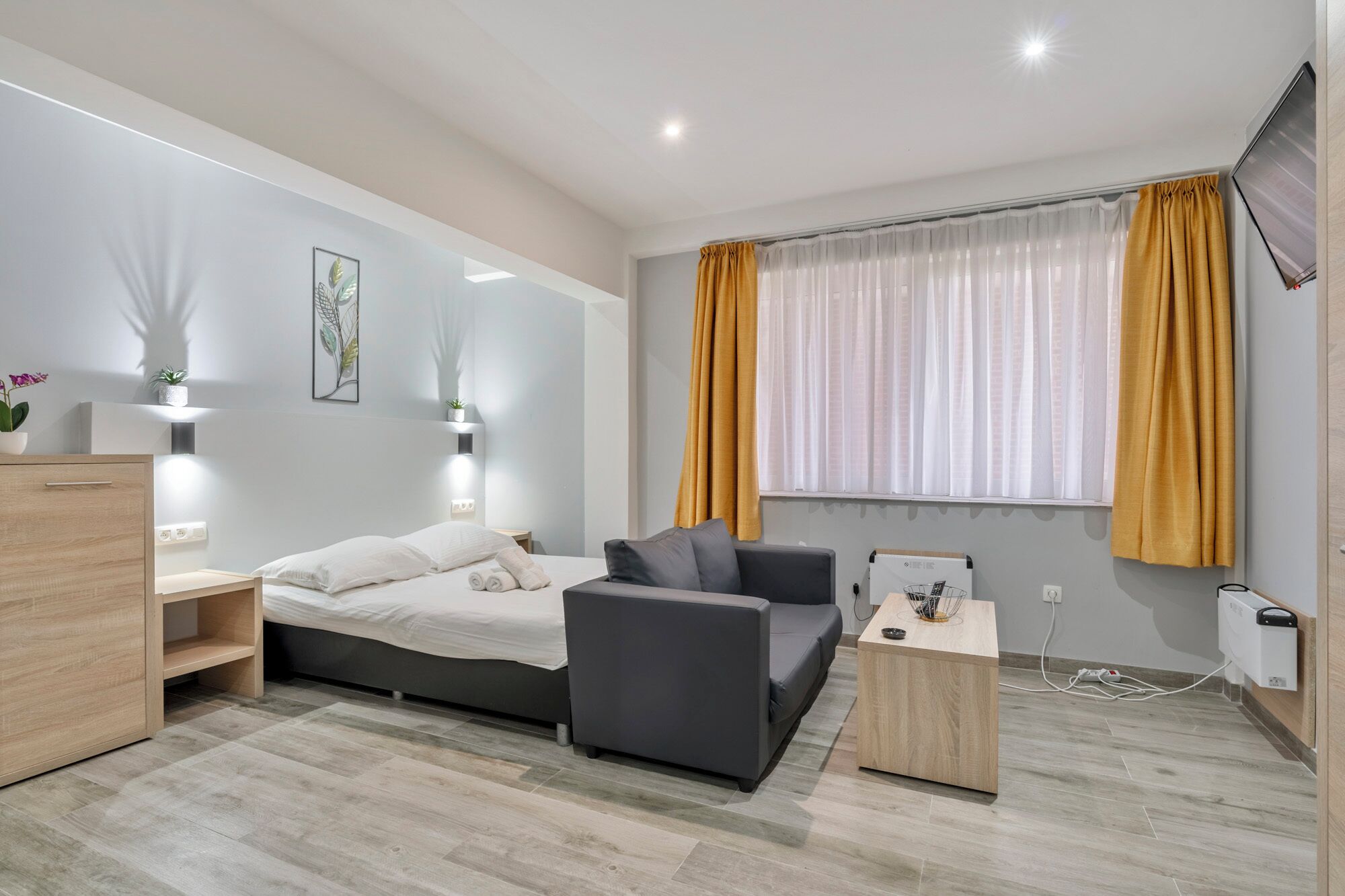 Quarto de hotel moderno com uma cama, um sofá, uma escrivaninha e uma televisão.