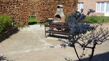 A courtyard with a bench, a sculpture, and a hedge.