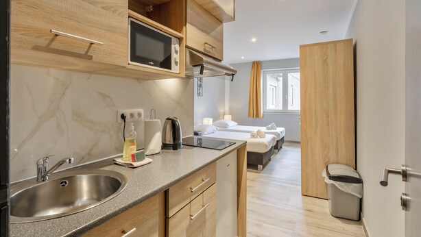 A modern hotel room with a kitchen area, a bed, and a bathroom. - Budget Flats Leuven (Leuven)