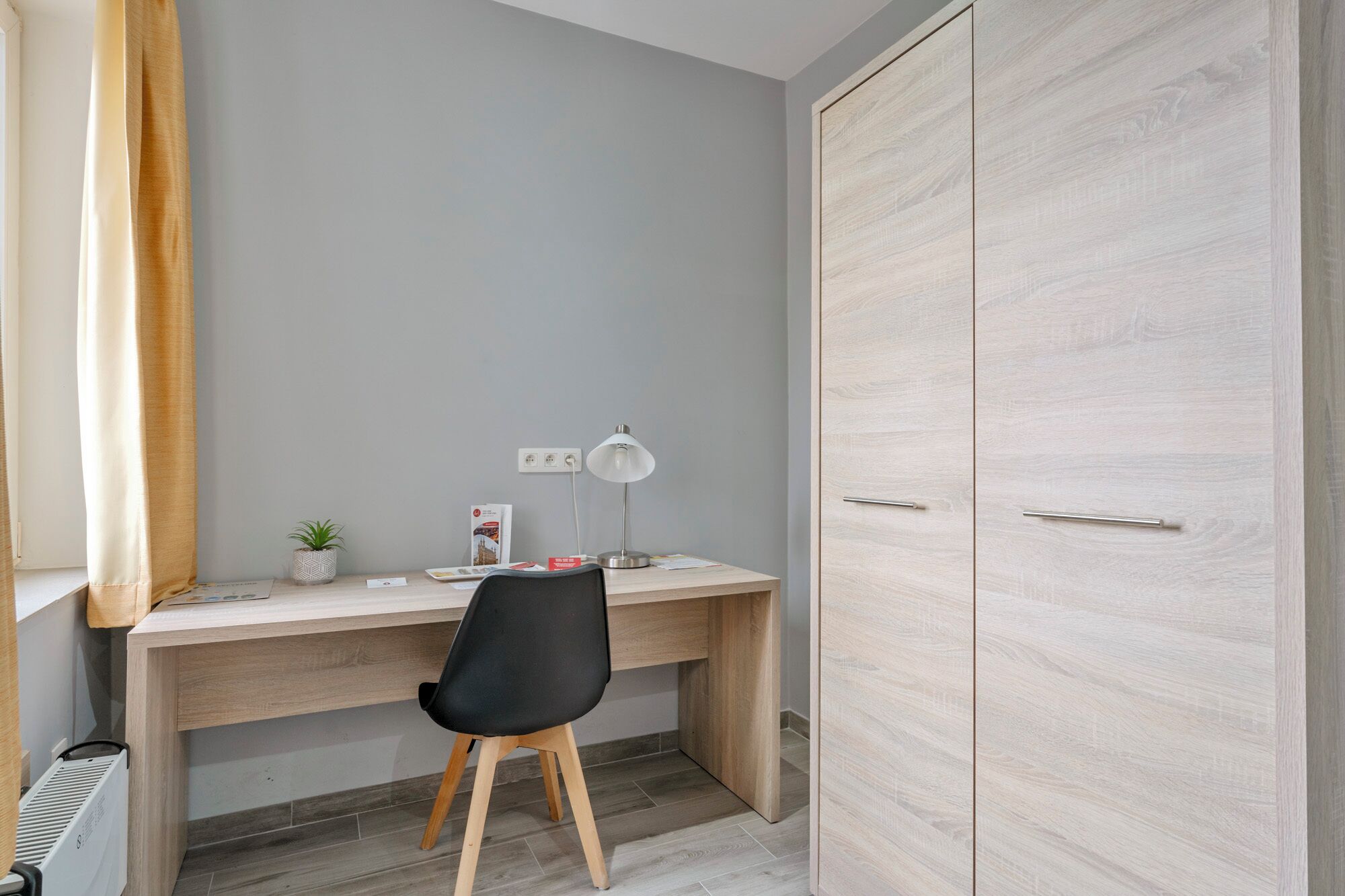 Un petit bureau comprenant un bureau, une chaise, une lampe et une armoire.