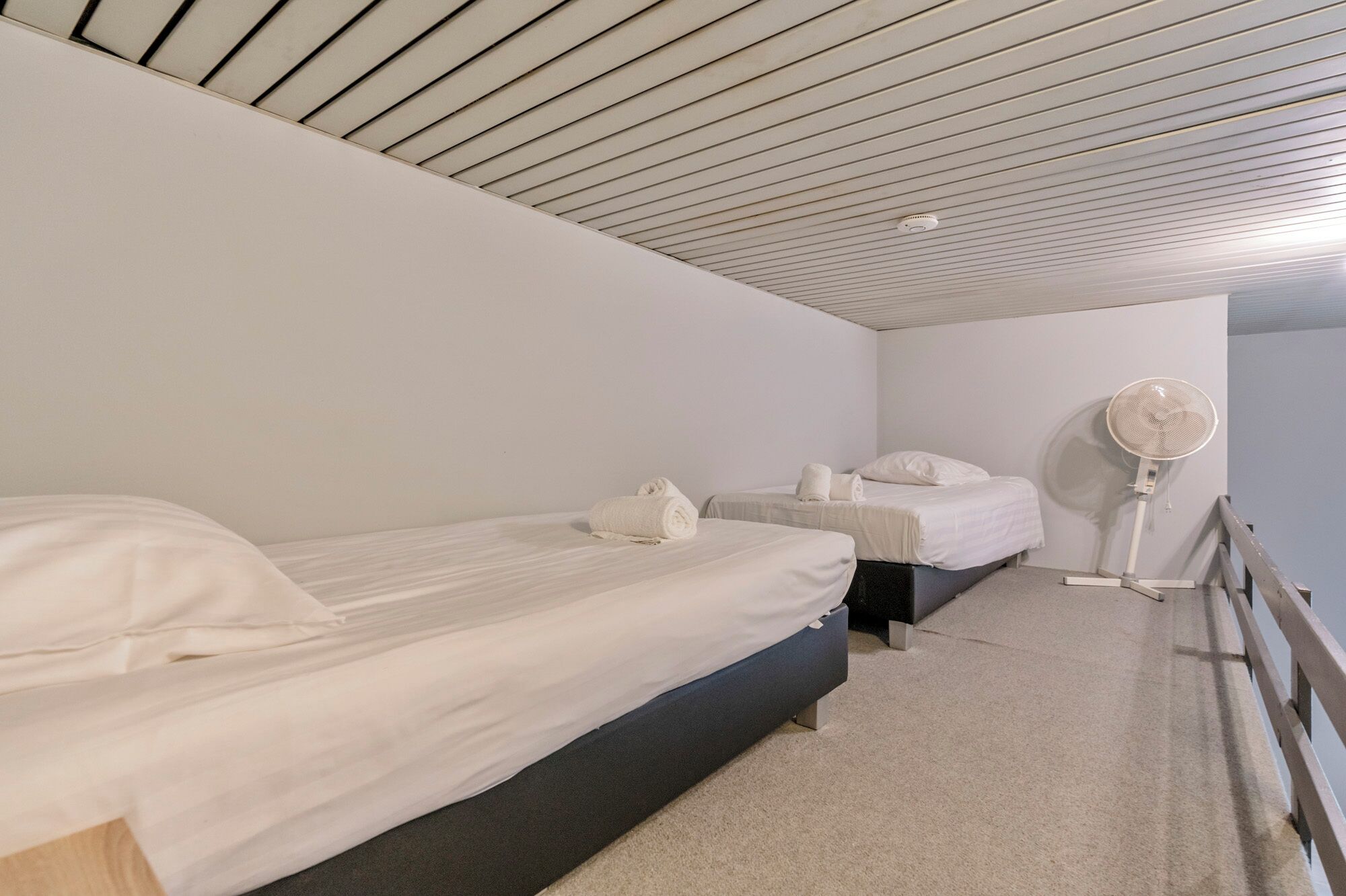 Una habitación con dos camas, un ventilador de pie y un techo de listones.