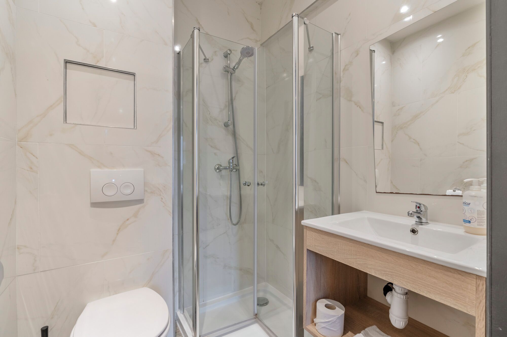 Une salle de bain moderne avec une douche à parois de verre, des toilettes, un lavabo avec un miroir et un mur recouvert de carreaux de marbre.