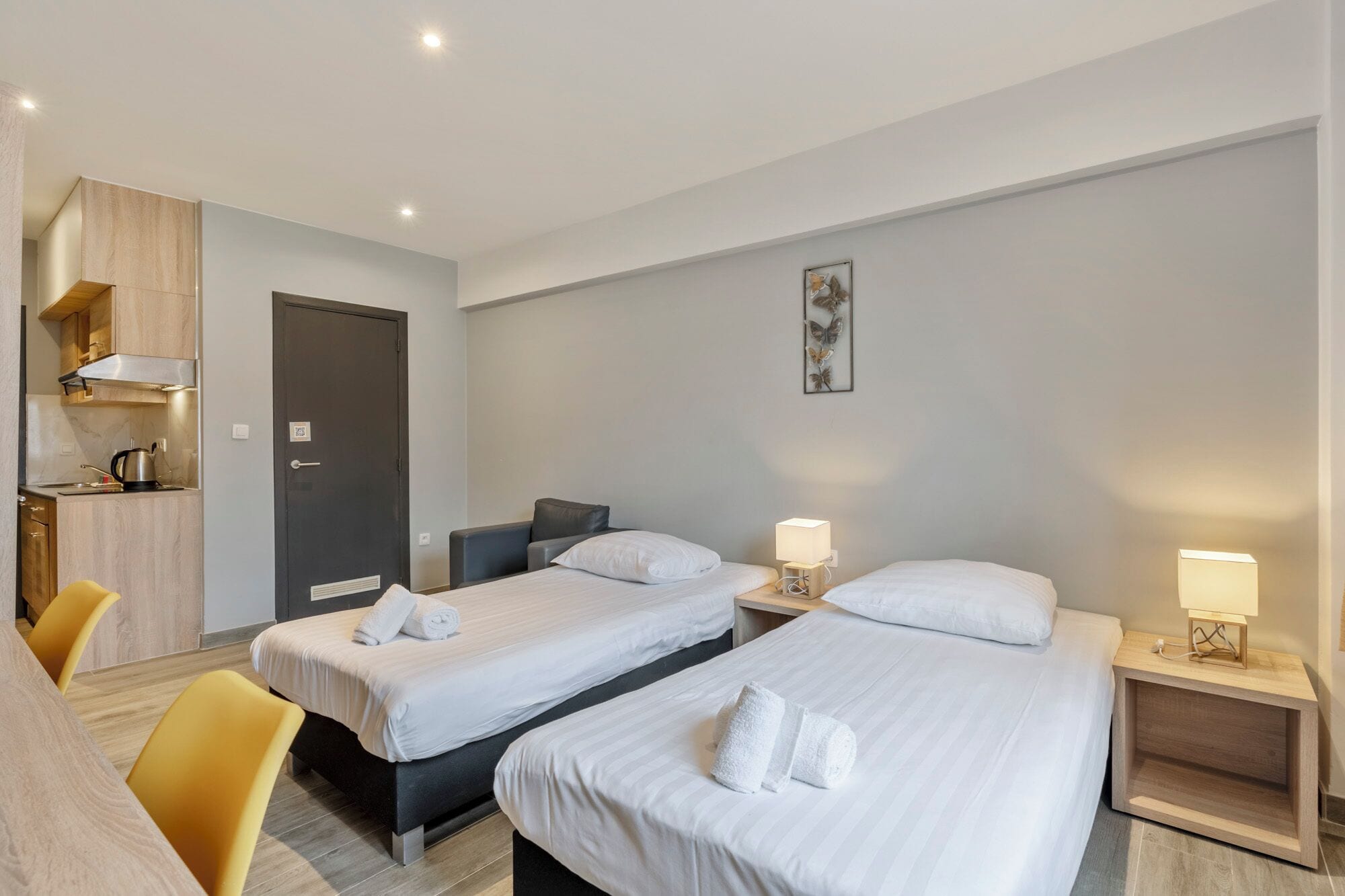 A hotel room with two single beds, a small kitchenette, and a dining area with yellow chairs.
