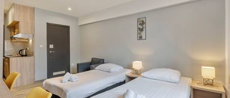 A hotel room with two single beds, a small kitchenette, and a dining area with yellow chairs.