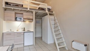 A compact kitchen with a built-in microwave, a small refrigerator, and a sink. A white ladder leads to a lofted sleeping area. - Budget Flats Leuven (Leuven)