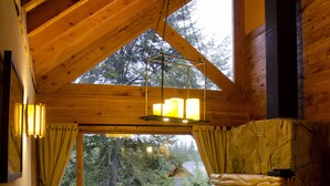 A cozy cabin interior with a stone fireplace, wooden ceiling beams, a sofa, and a dining table. - Tillka, Casas de Montaña (Villa La Angostura)