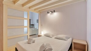 Un dormitorio con cama, dos mesitas de noche, una lámpara de pared y una puerta corredera con paneles de vidrio esmerilado.