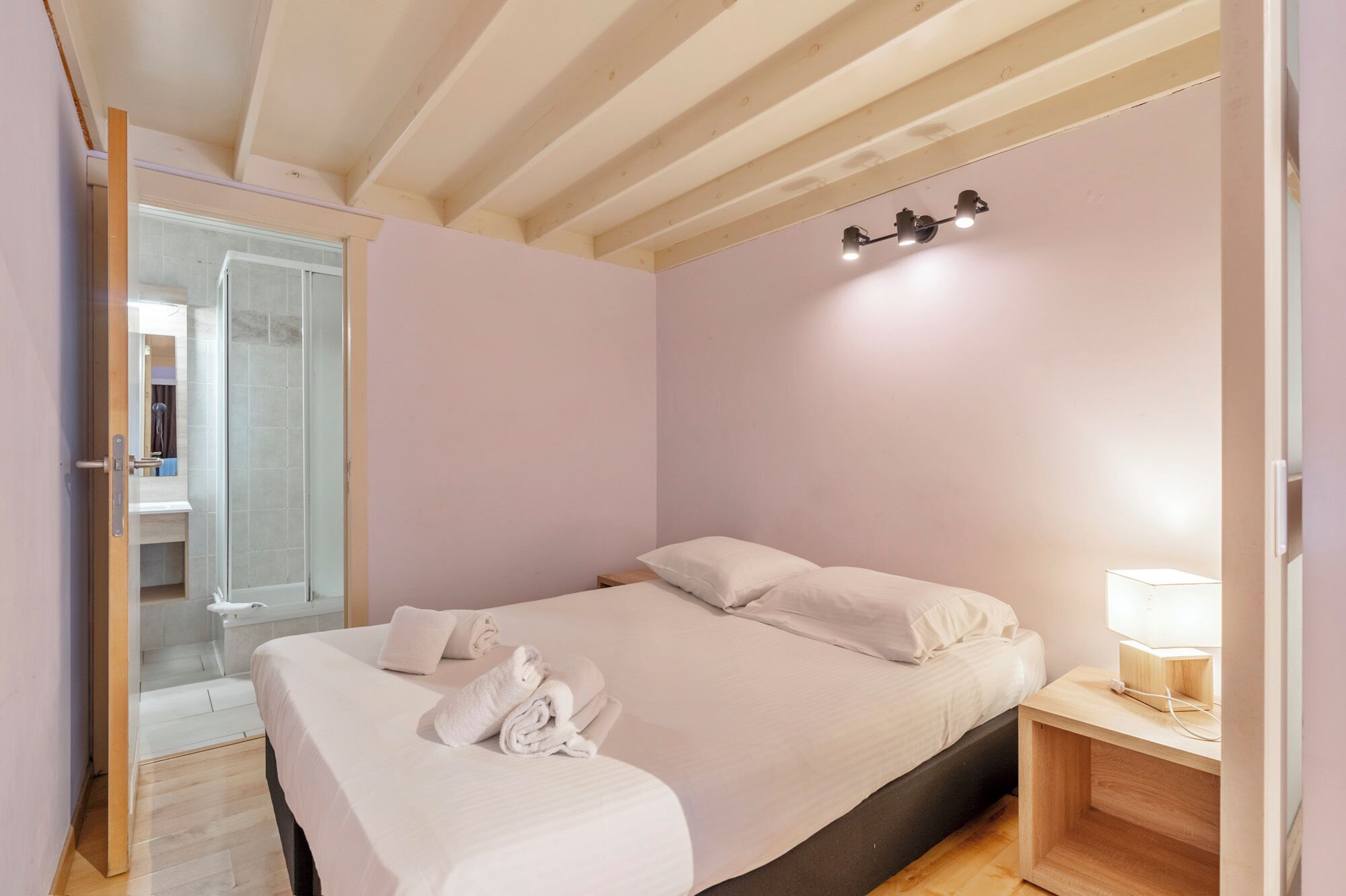 A bedroom with a bed, a bedside table with a lamp, and a wooden ceiling.