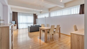 Una sala de estar moderna con comedor, piso de madera y ventanas grandes con cortinas.