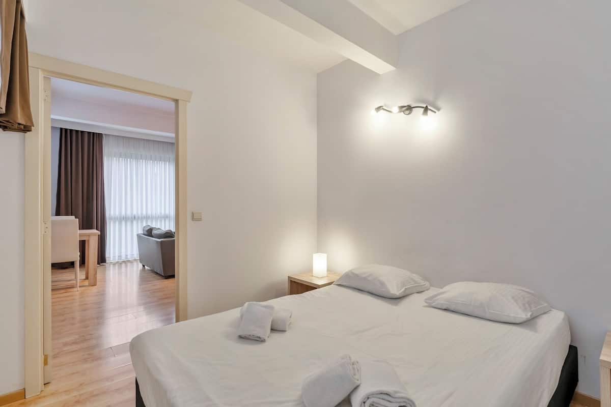 Une chambre d’hôtel avec un lit, une table de chevet, une lampe et une vue sur un balcon et une autre pièce.