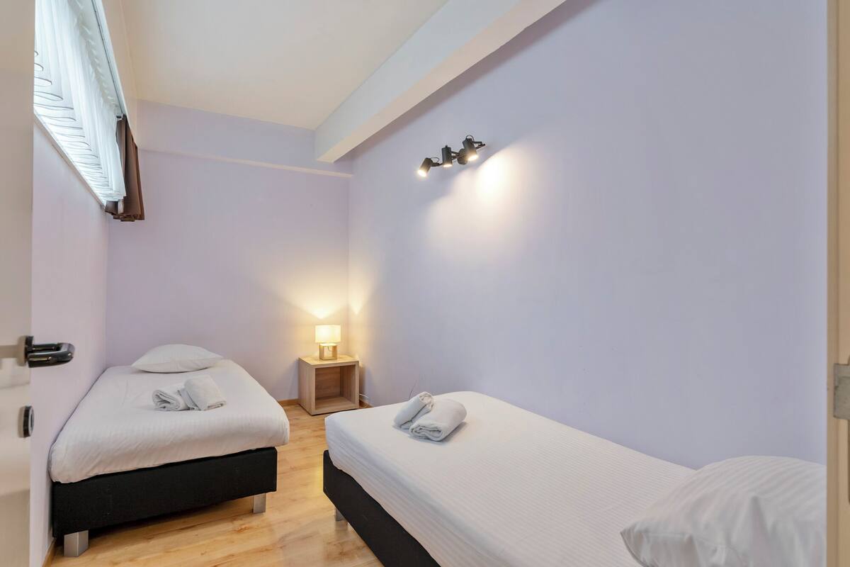 Une chambre d’hôtel avec deux lits, une table de chevet avec une lampe et un luminaire au plafond.