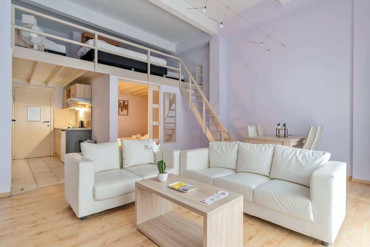 Un salon moderne et bien éclairé, comprenant un ensemble de canapés, une table basse et un lit superposé avec une échelle.