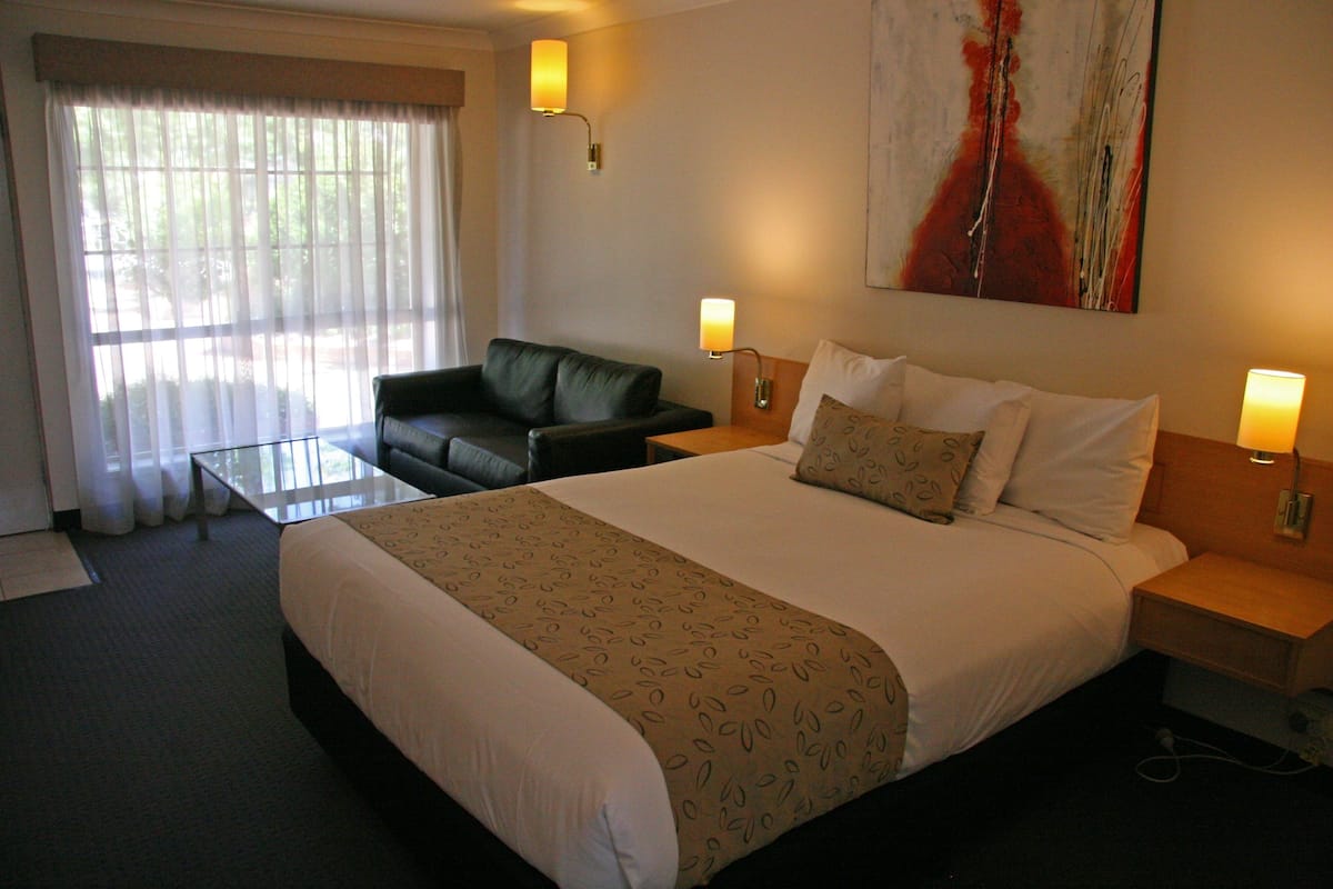 A hotel room with a large bed, a small sofa, a coffee table, two bedside lamps, and a painting on the wall.