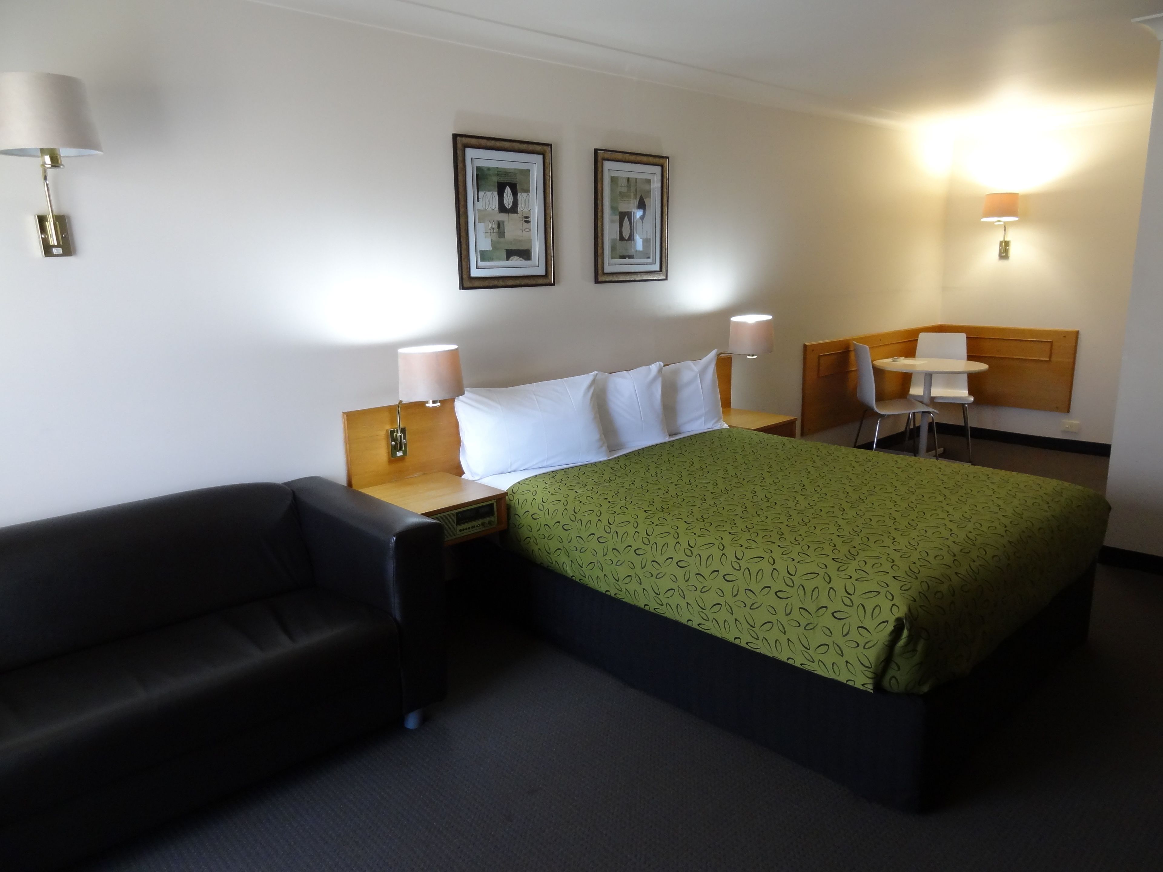Een hotelkamer met een bed, een stoel, een bureau en twee wandlampen.