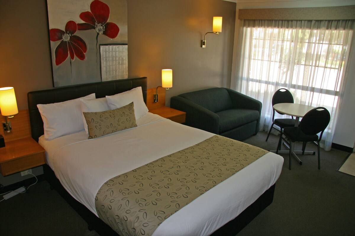 A hotel room with a large bed, a desk, a chair, and a window with curtains.