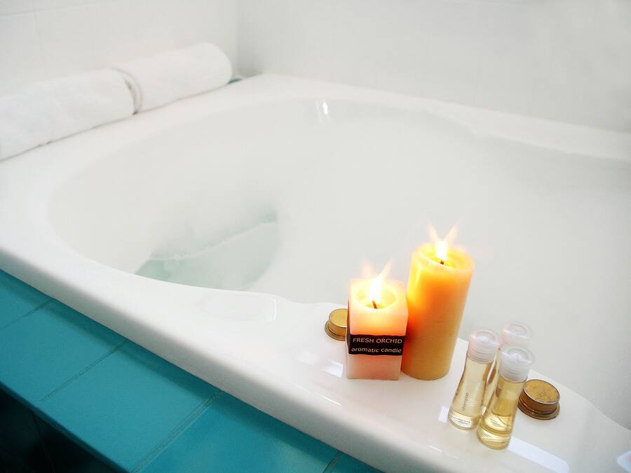 Una bañera con dos velas encendidas y tres botellas de líquido.