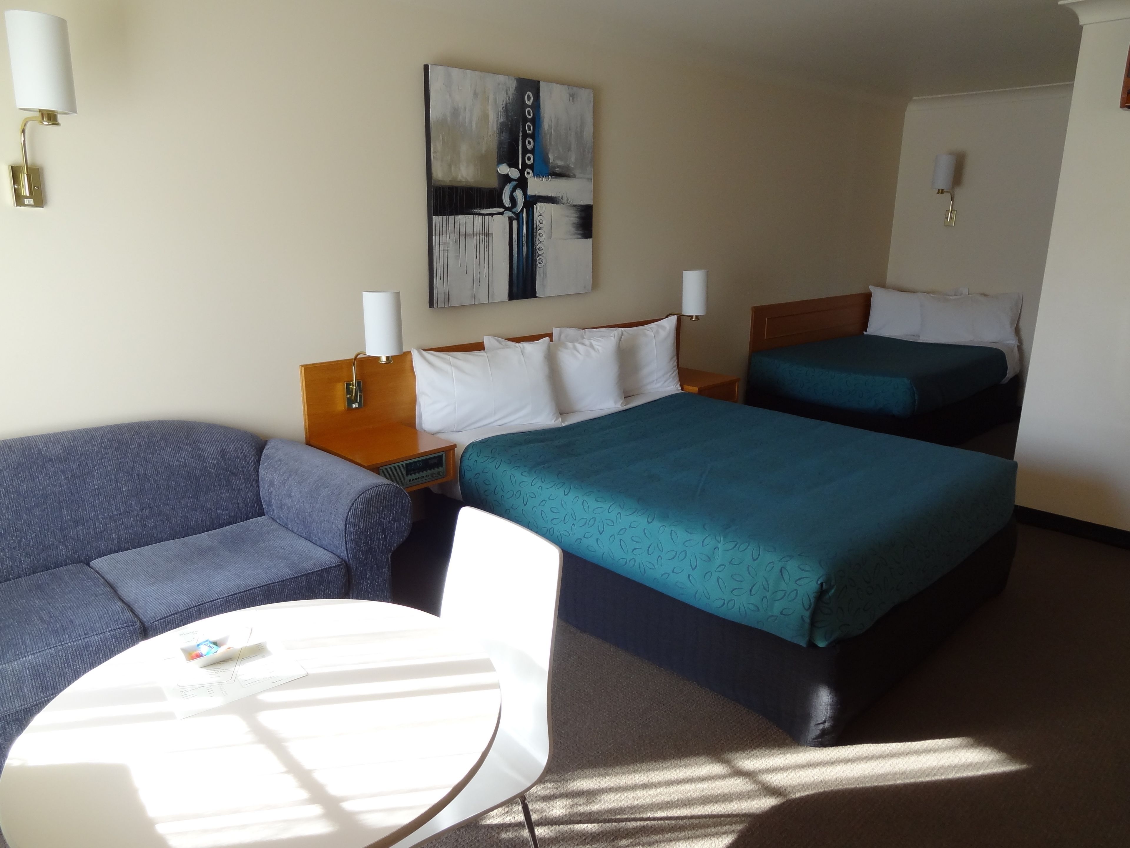 Habitación de hotel con sofá, dos camas individuales, una mesita y un cuadro en la pared.