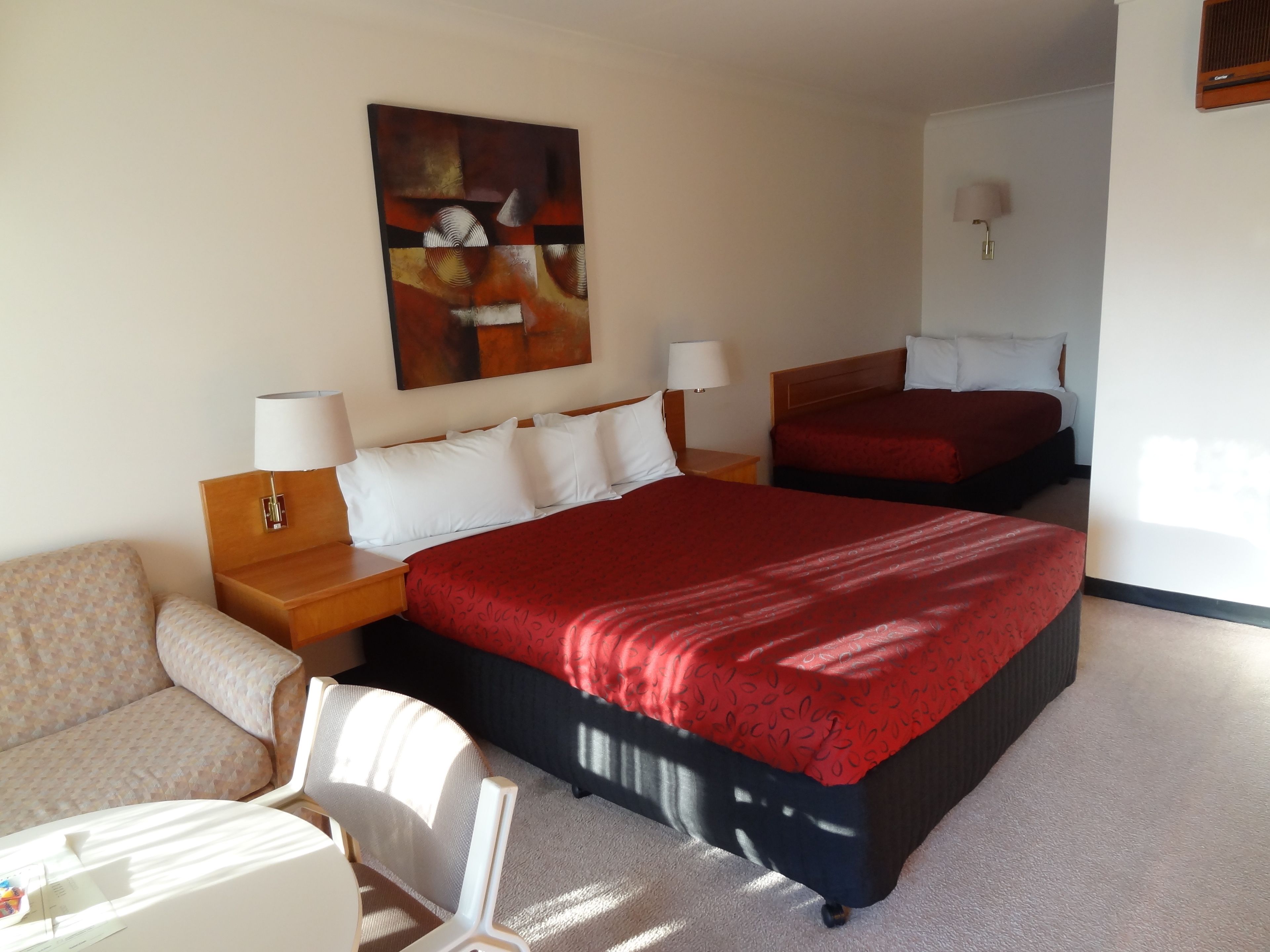 A hotel room with two beds, a sofa, a desk, and a painting on the wall.