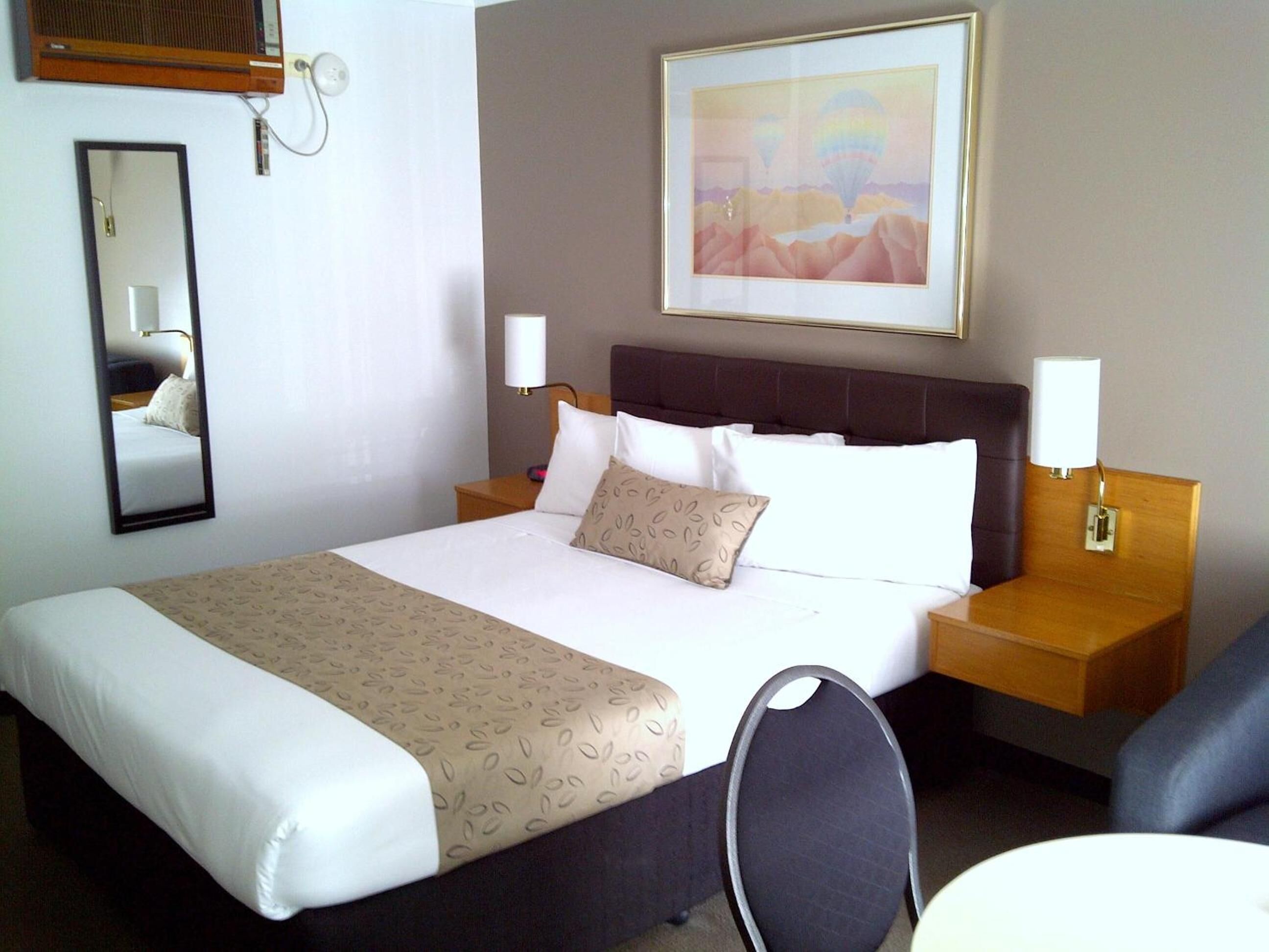 Une chambre d’hôtel avec un grand lit, deux tables de chevet, une chaise, un miroir et un tableau au mur.