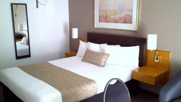 Une chambre d’hôtel avec un grand lit, deux tables de chevet, une chaise, un miroir et un tableau au mur.
