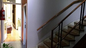 A staircase with a wooden handrail and glass balustrade, leading to a landing with a potted plant and a bench. - Hotel Chipre (Buenos Aires)