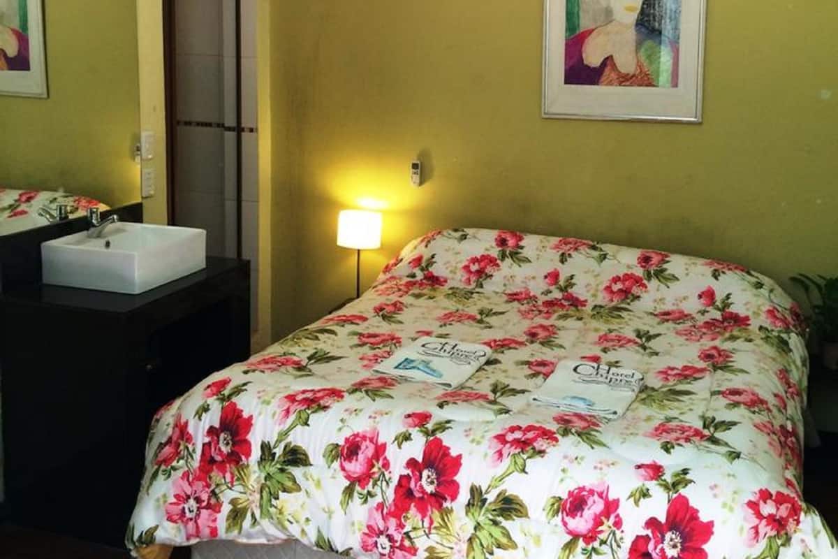A hotel room with a bed, a bedside table, a sink, and a mirror.