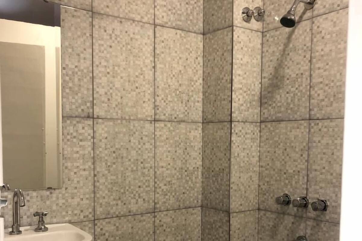 A bathroom with a sink, mirror, shower, and tiled walls.
