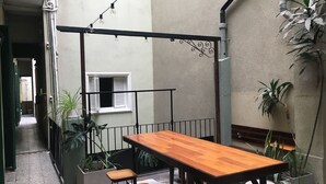 A small, enclosed outdoor dining area with a wooden table and four stools, surrounded by potted plants and a metal railing. - Hotel Chipre (Buenos Aires)