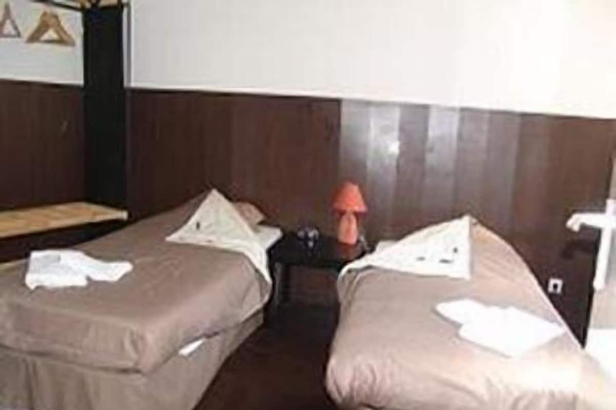 A hotel room with two beds, a nightstand, and a lamp.