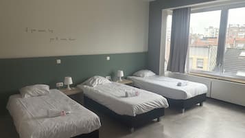 A hotel room with three beds, a window with curtains, and a wall with a motivational quote.