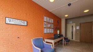 A reception area with a brick wall, a 'Welcome to our home' sign, framed certificates, a reception desk, two chairs, and a door in the background. - Budget Flats Antwerpen (Antwerp)