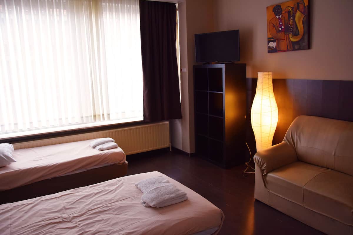 A hotel room with two single beds, a sofa, a TV, and a lamp.