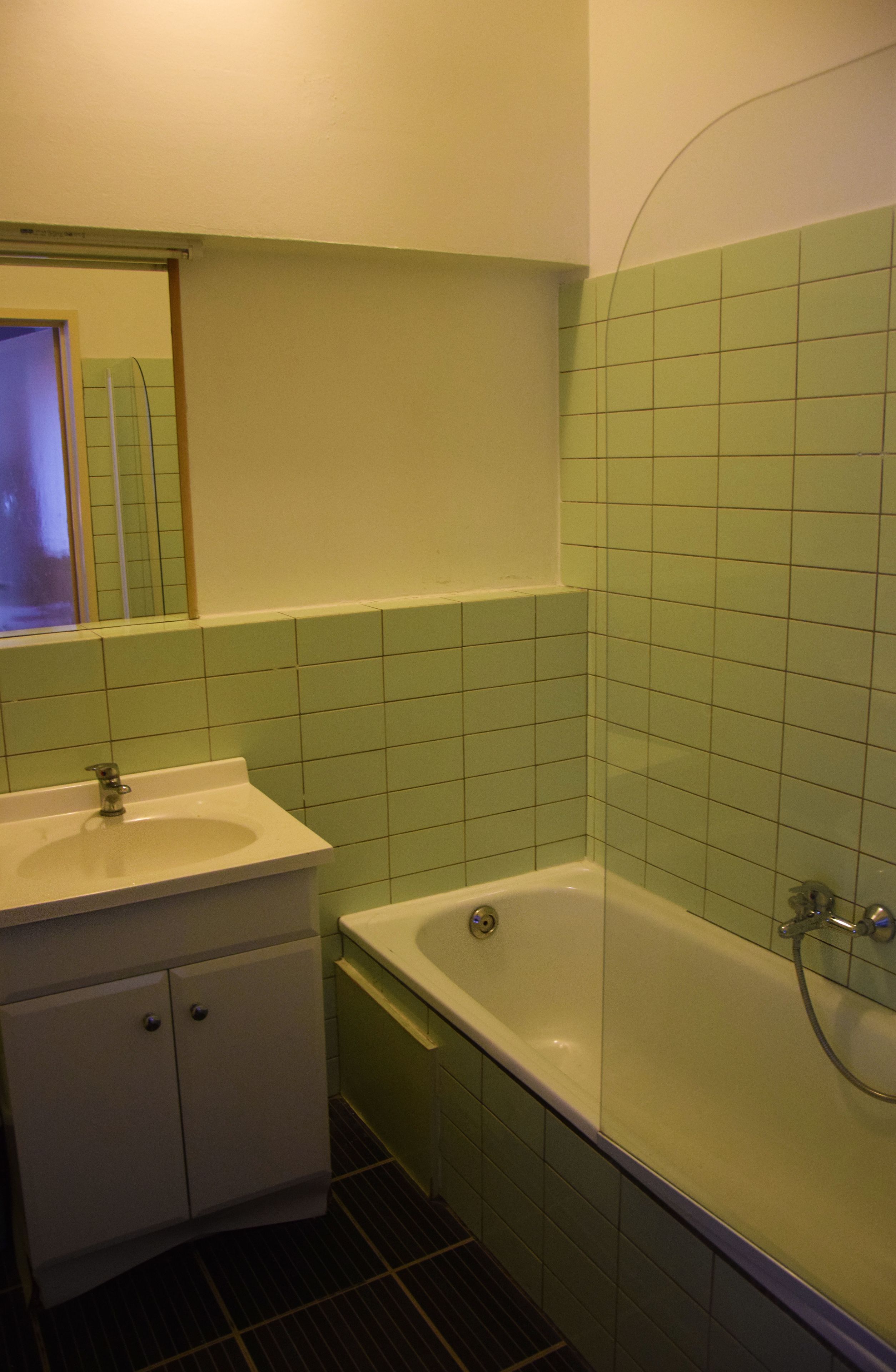 Ein Badezimmer mit weißem Waschbecken, einem Spiegel, einer Badewanne und grünen Fliesenwänden.