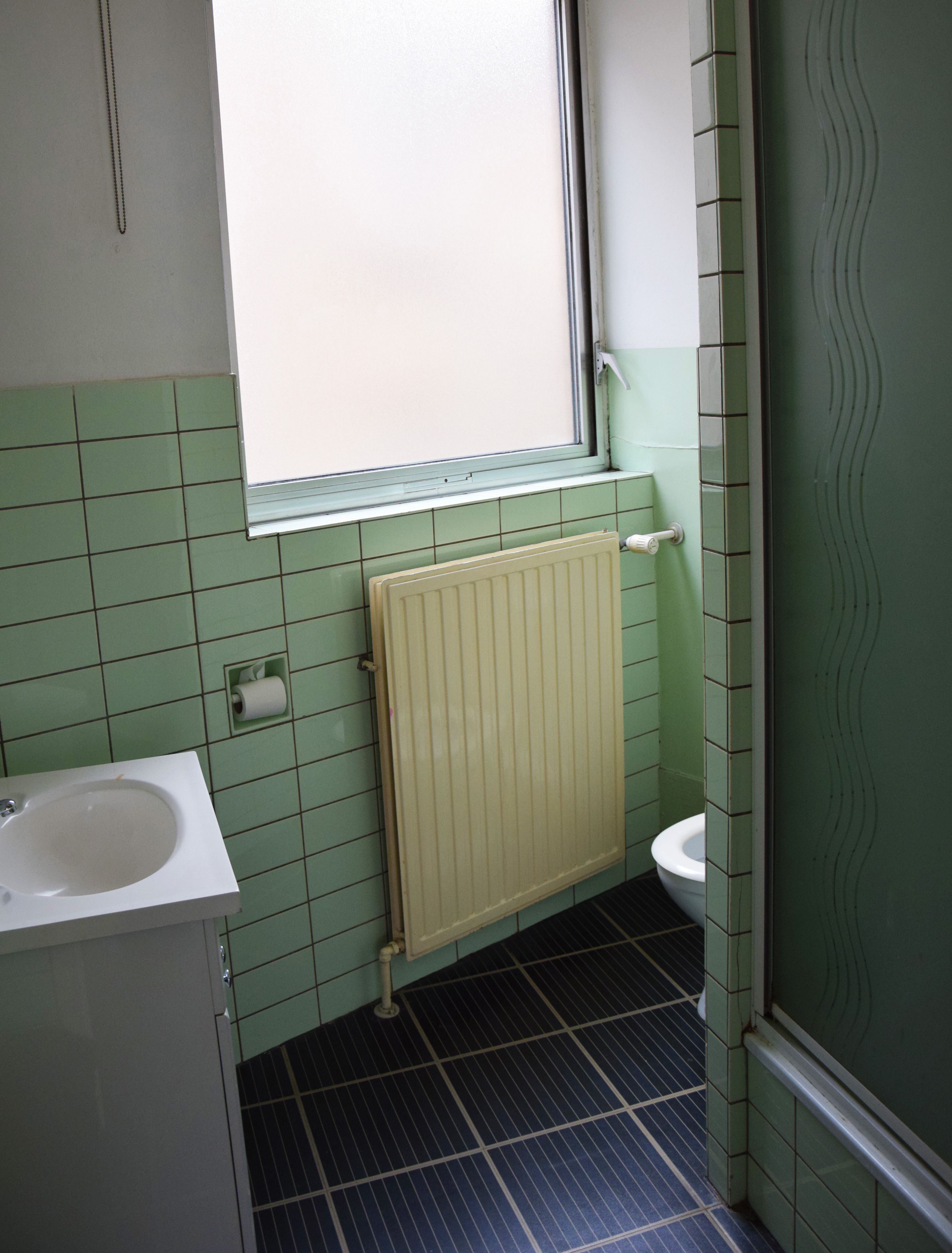 Een badkamer met een raam, een radiator, een wastafel en een toilet.
