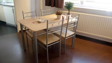 A dining area with a wooden table and metal chairs, a potted plant, and a window with curtains.