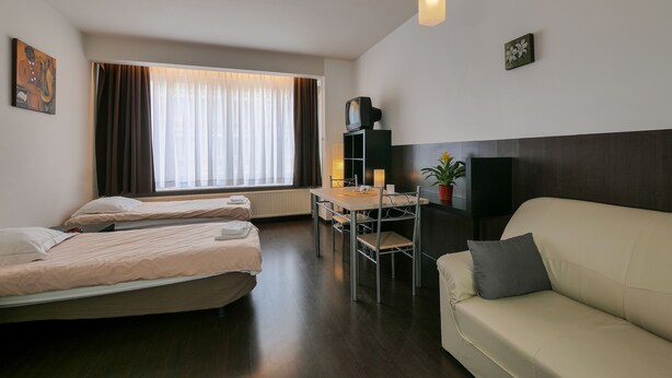 A modern hotel room with two beds, a dining table, a sofa, and a TV. - Budget Flats Antwerpen (Antwerp)