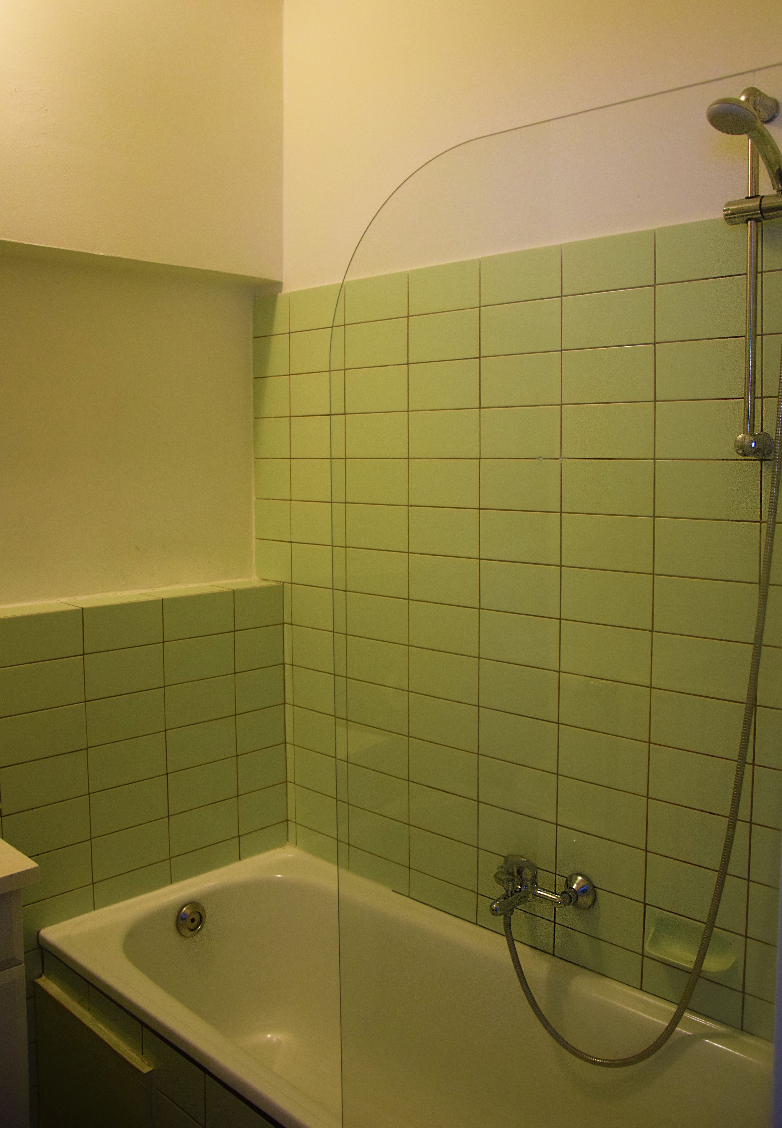 Un baño con bañera y ducha, paredes de azulejos verdes y un lavamanos blanco.