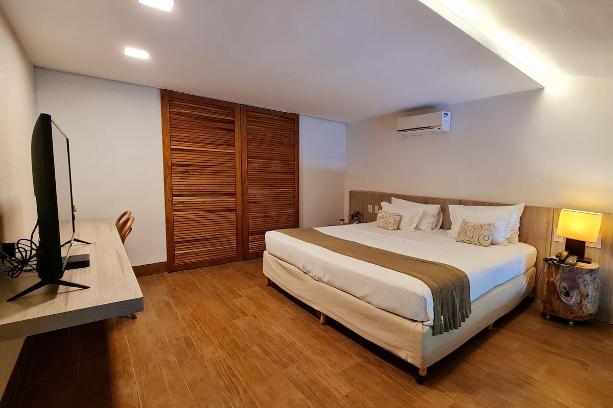 Una habitación de hotel moderna con una cama grande, armario de madera y un escritorio con computadora.