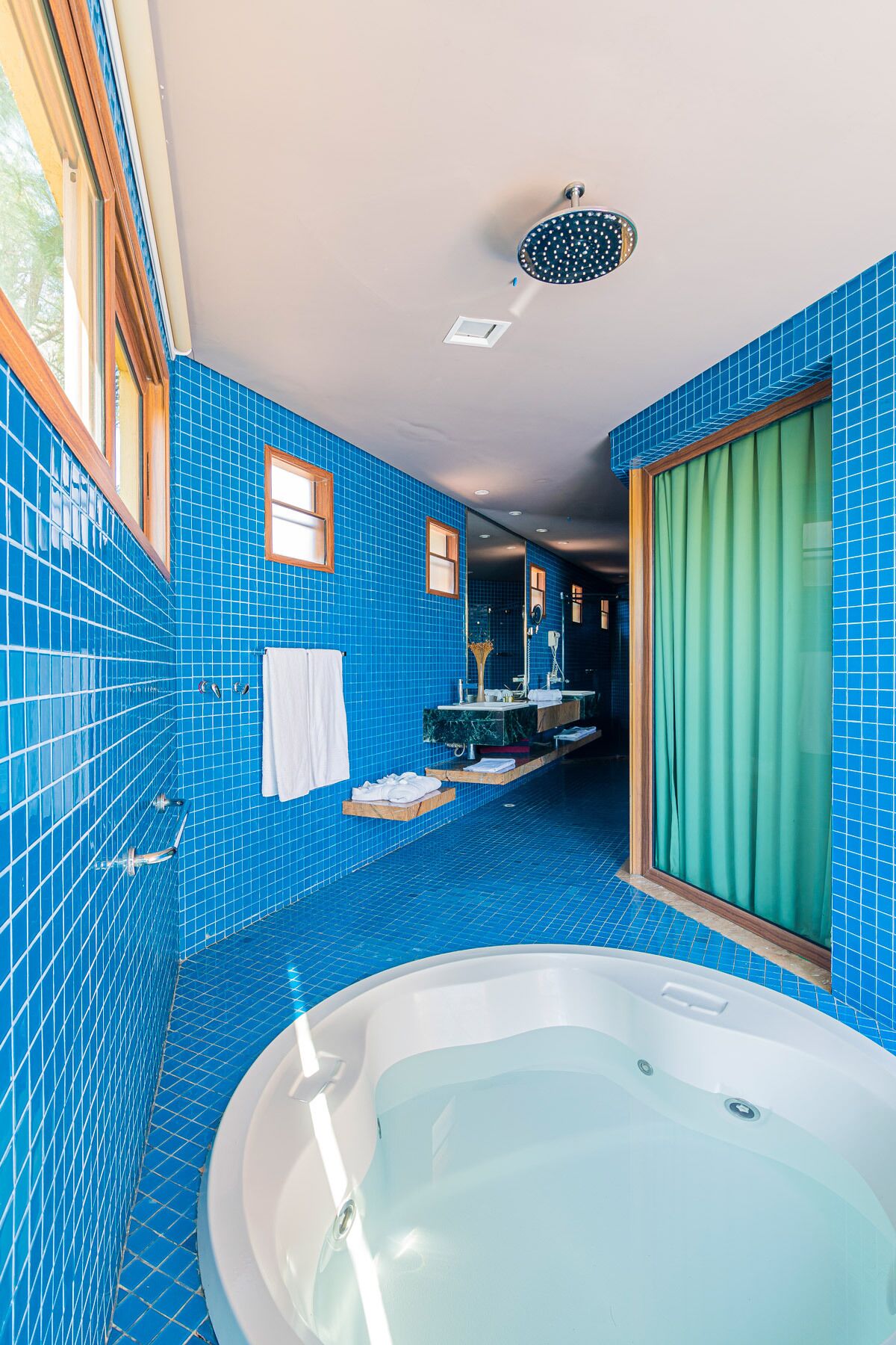 A bathroom with blue-tiled walls, a large bathtub, a shower, and a vanity with a mirror.