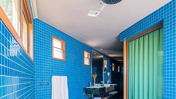 A bathroom with blue-tiled walls, a large bathtub, a shower, and a vanity with a mirror.