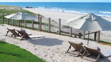 A beachside lounge with wooden lounge chairs and umbrellas, overlooking the ocean.