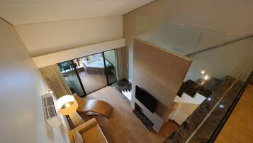 A modern living room with a flat-screen TV, a sofa, a coffee table, and a glass door leading to a balcony with a hot tub.