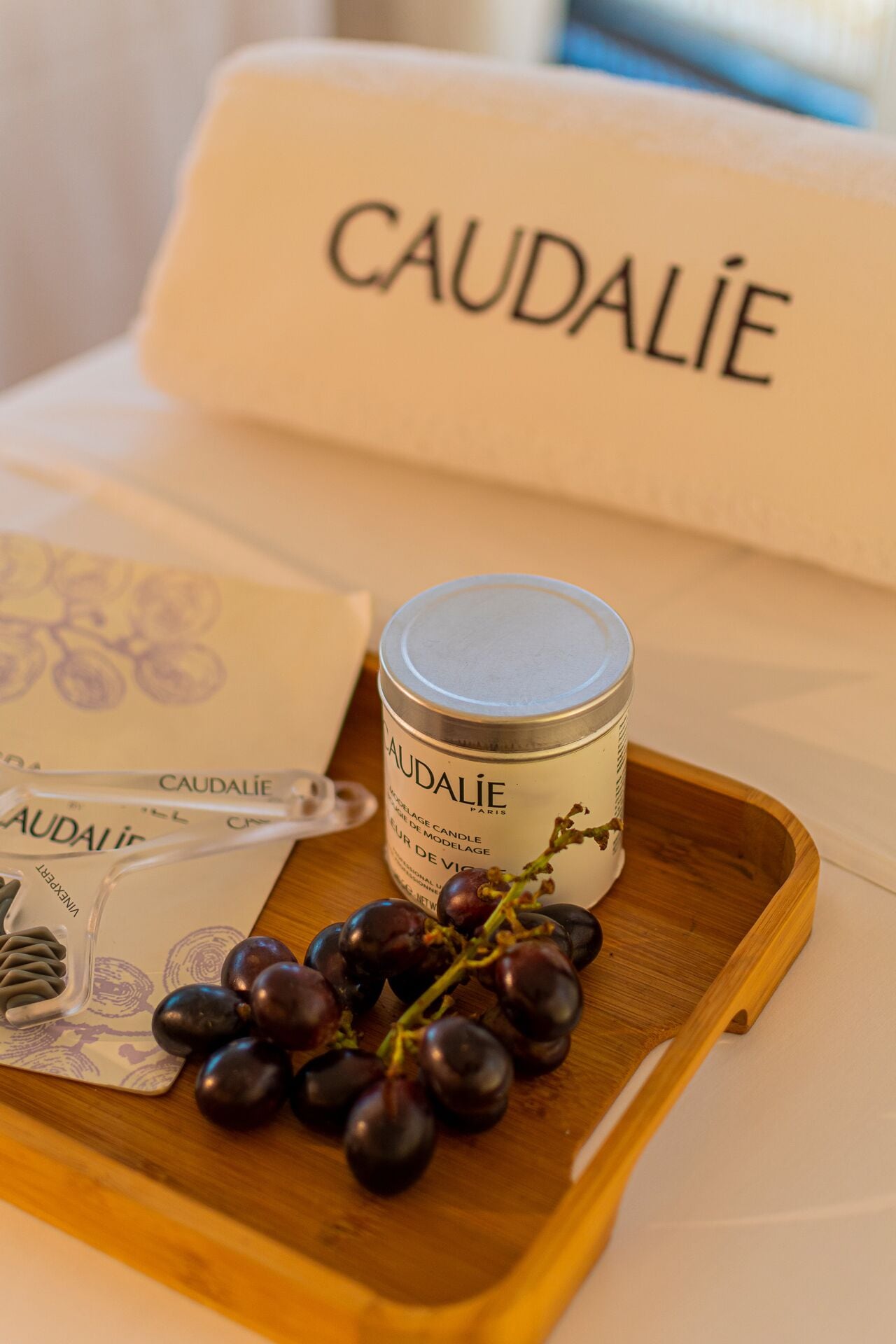 A candle, a bunch of grapes, and a pillow with the word "CAUDALIE" on it.