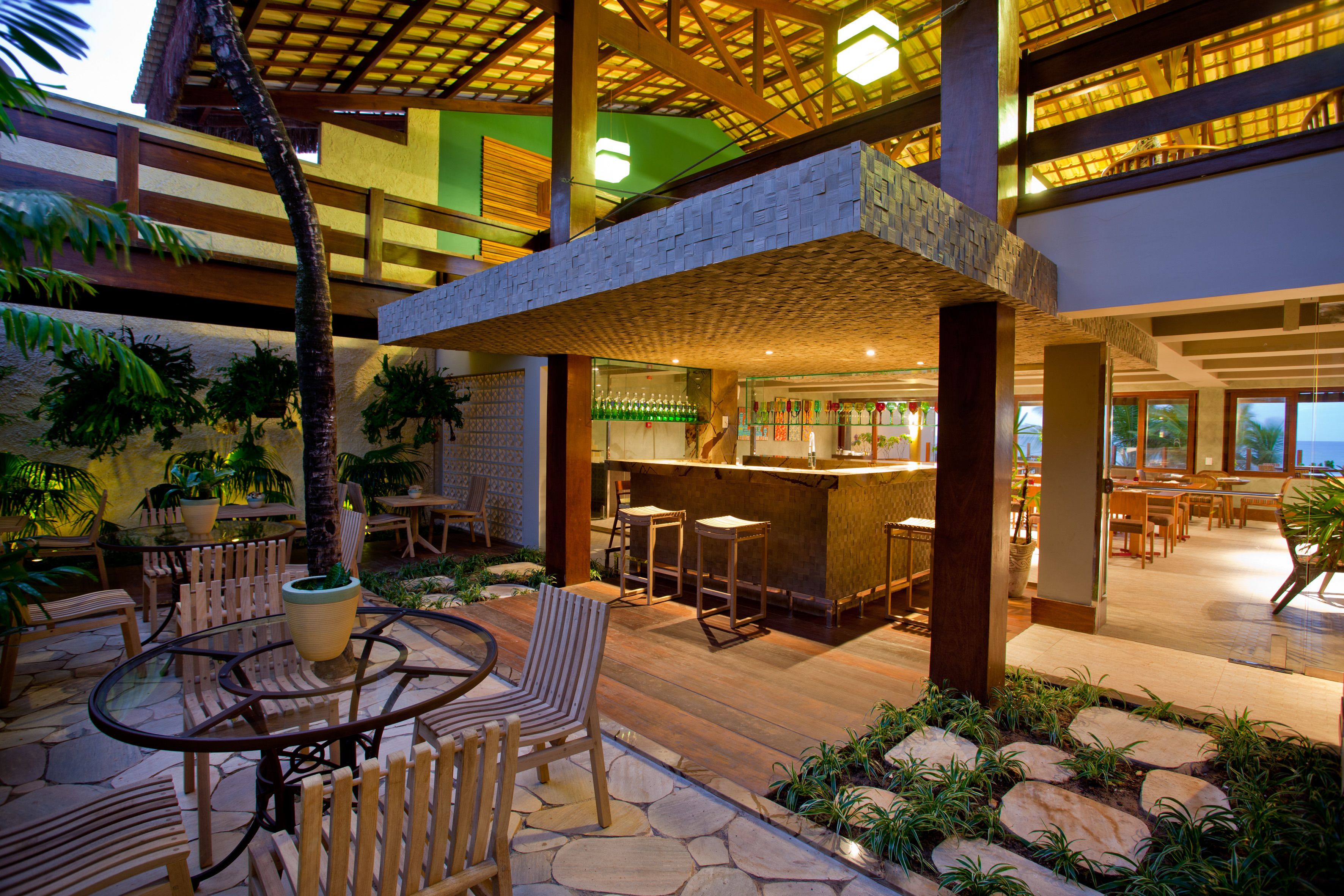 Un espacio al aire libre para comer con varios niveles, suelo de piedra, mobiliario de madera y una zona de bar con taburetes.